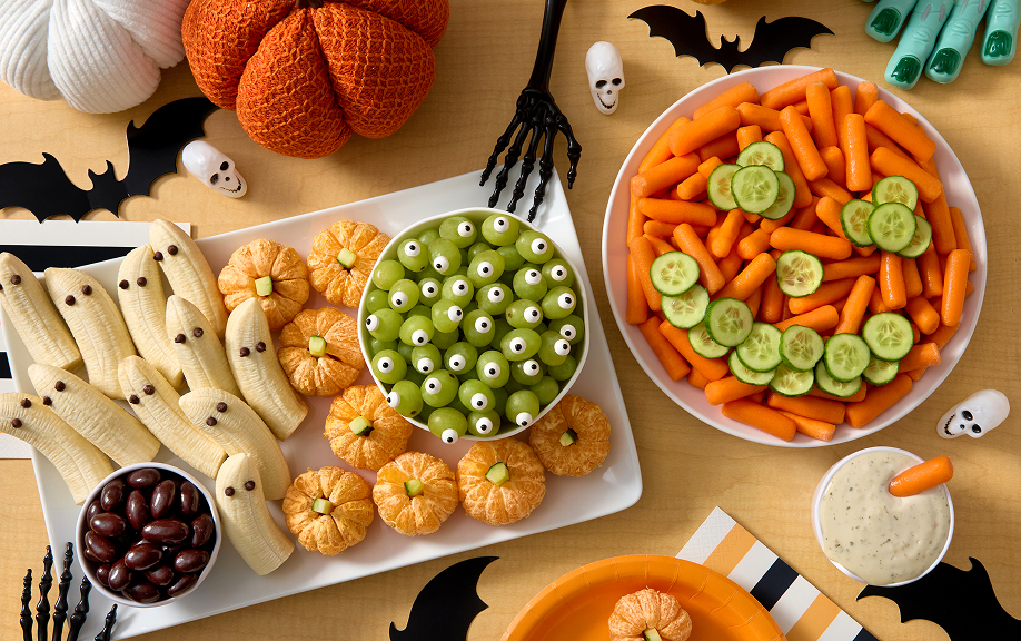 Halloween snack spread — banana ghosts, pumpkin treats, grapes, carrots, cucumbers and dip