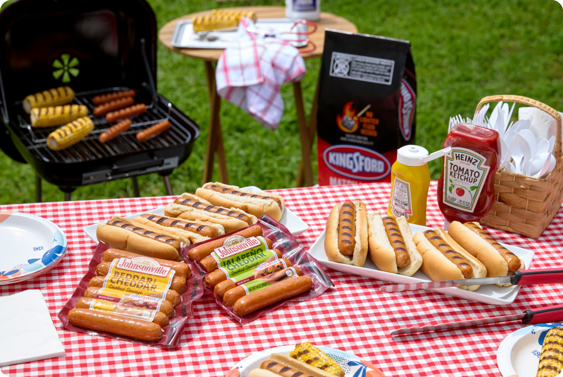 Grilled hot dogs cookout featuring Johnsonville smoked sausage, charcoal, ketchup and mustard outdoors